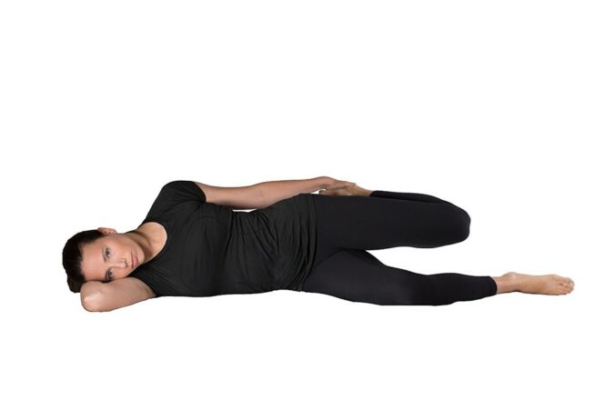 Woman doing a quad stretch lying on right side while holding left foot pinned to butt