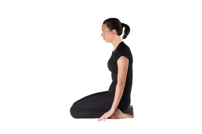 Woman doing quad stretch while kneeling, sitting back onto a yoga block resting on the ground between her feet