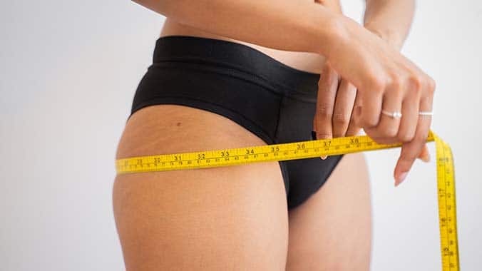 Woman measuring hip circumference with flexible measuring tape